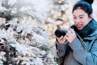 Woman holding a camera next to a fake snowy christmas tree
