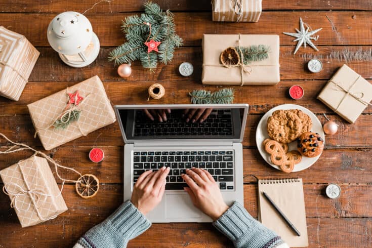 Hands typing at a laptop computer, surrounded by cookies, decorations and wrapped gifts.