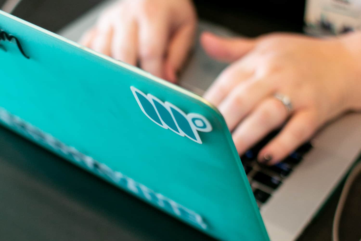 someone typing on laptop with a teal cover and mediavine stickers