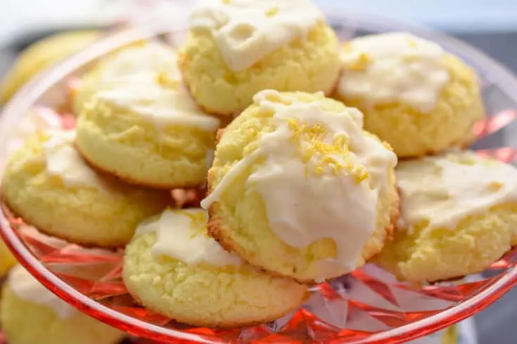 A small pile of frosted sugar cookies sits on top of a red glass plate.