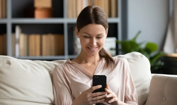 woman sitting on couch in home smiling at phone
