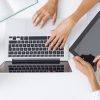 above view of 1 pair of hands typing on a laptop and another holding an ipad