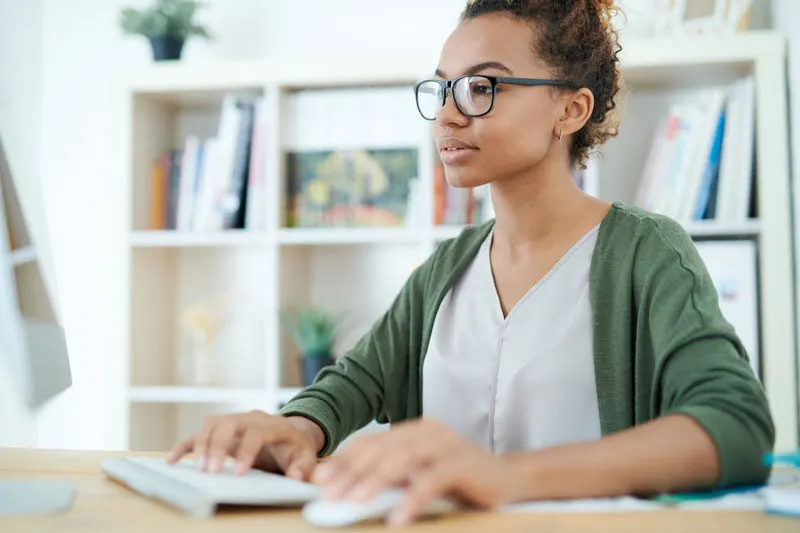 female developer wearing a green sweater and typing on a desktop computer in a home office