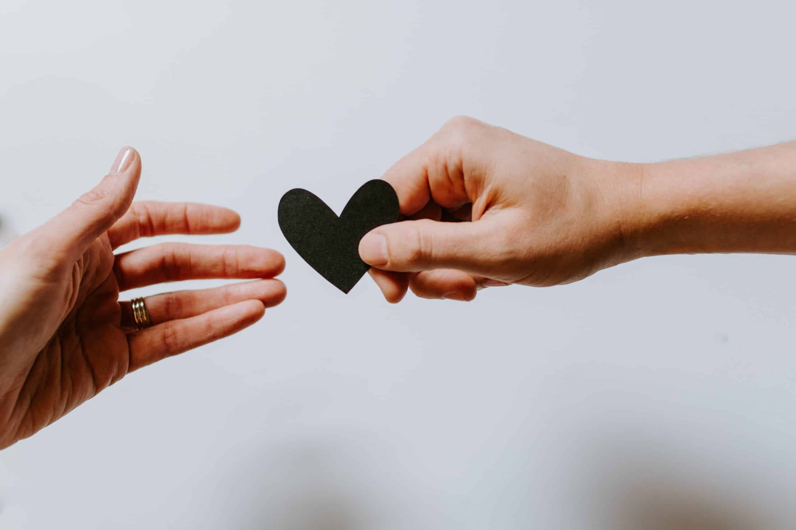 two people passing a black paper heart between two hands