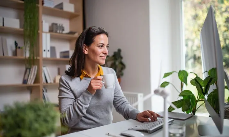 woman holding mug while typing with one hand smiling at computer screen