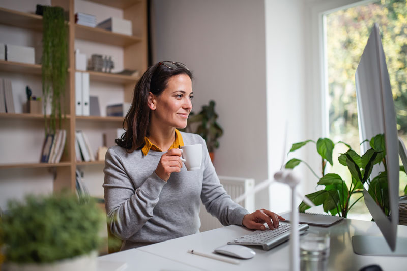 woman holding mug while typing with one hand smiling at computer screen