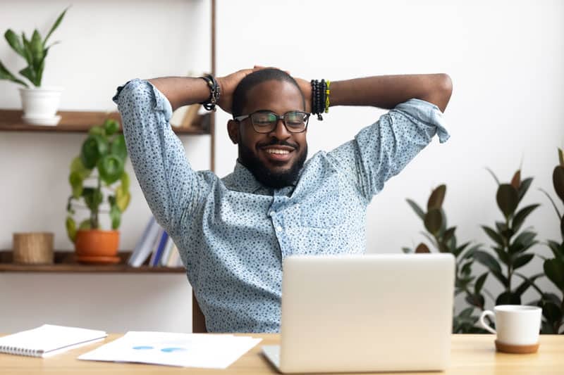 man smiling at his laptop computer in a home office with plants