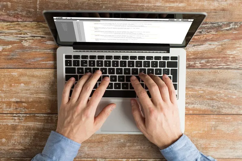 person in a blue shirt coding on a laptop computer