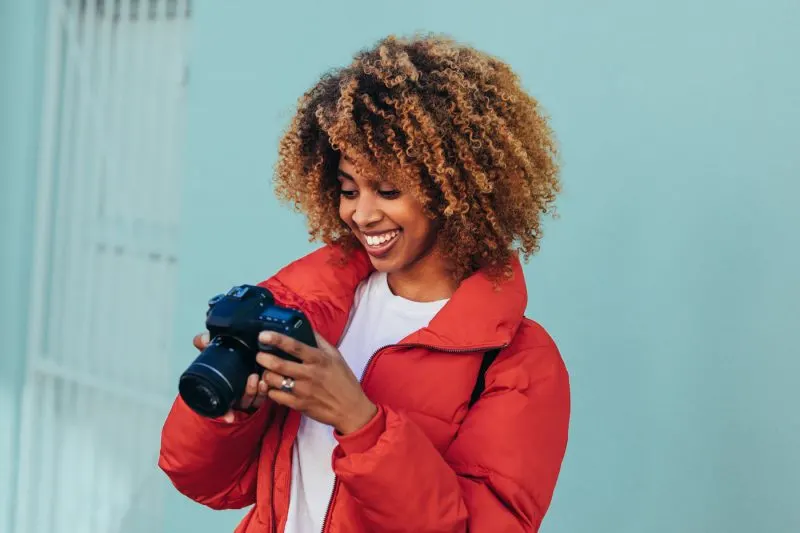 woman in red puffy jacket looking at photos on a DSLR camera in front of a blue building