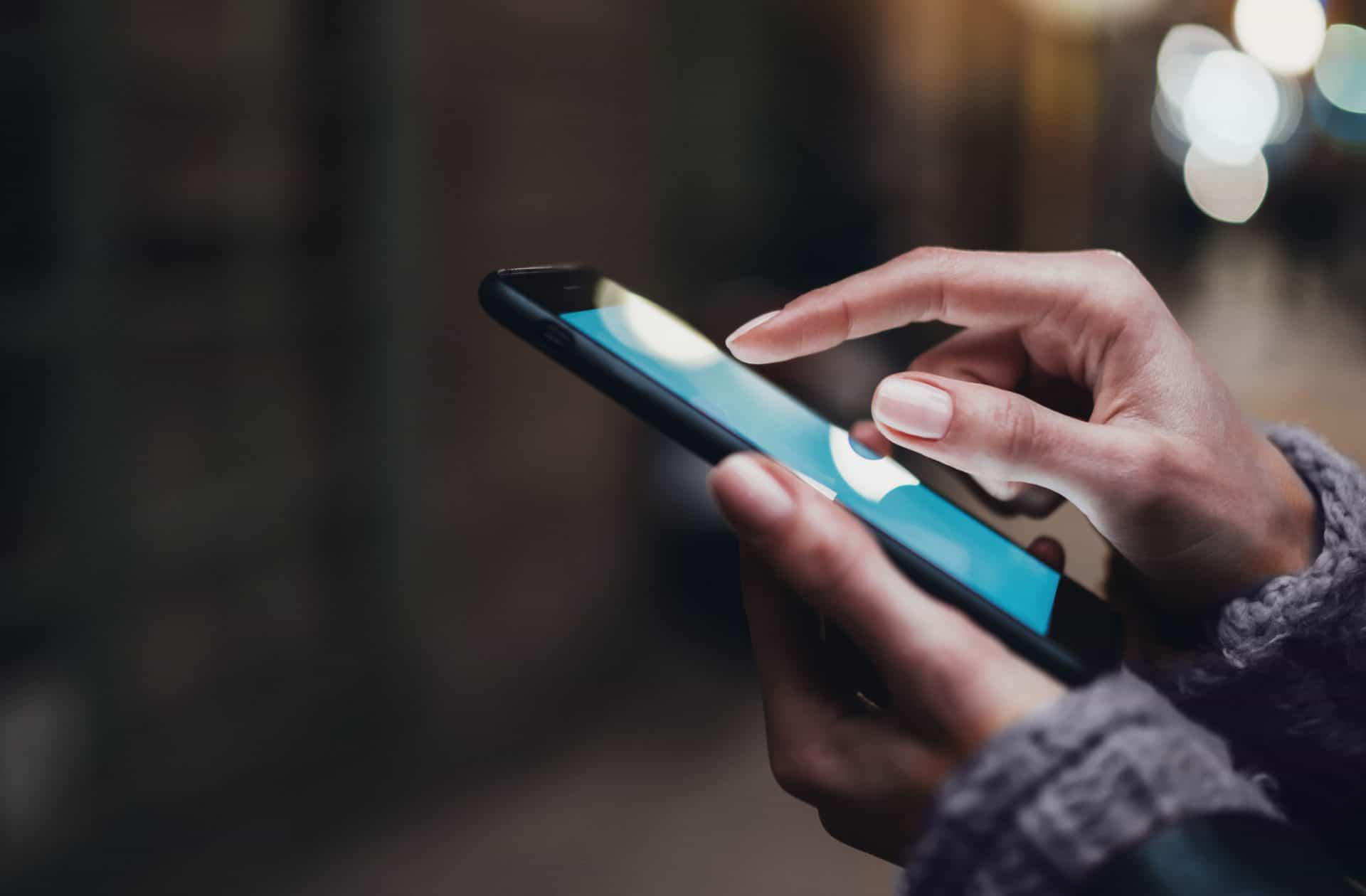 woman's hands scrolling a website on a mobile phone at night