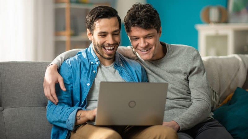 same-sex couple looking at a laptop on a couch