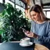 woman in gray shirt looking at social media on her smartphone in a coffee shop