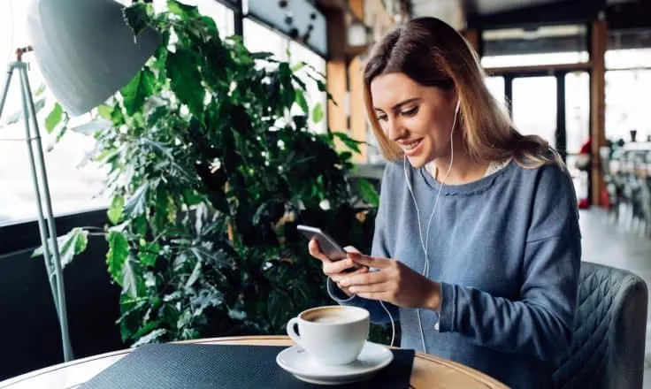 woman in gray shirt looking at social media on her smartphone in a coffee shop