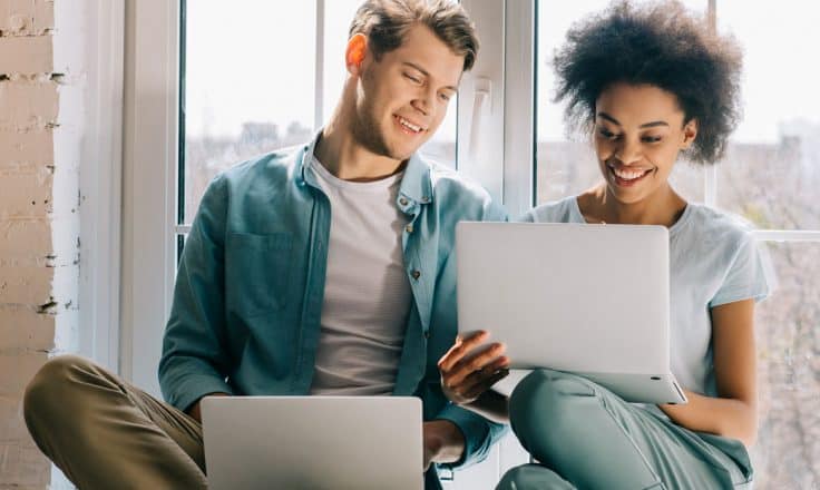 couple sitting in against an apartment window working together on their laptops