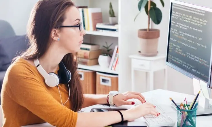 female developer wearing orange sweater coding from a desktop computer in a home office