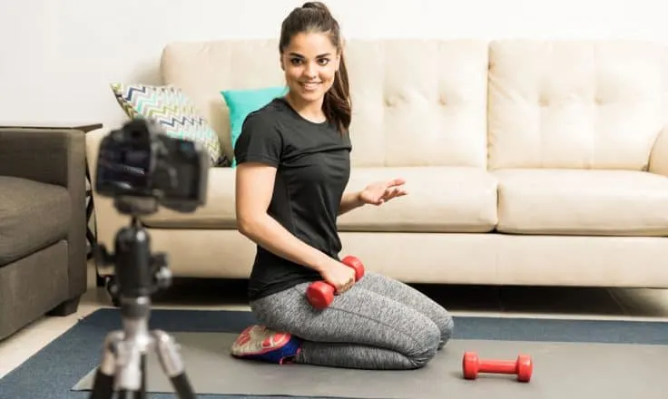 female fitness blogger filming an exercise video on a yoga mat in her living room