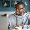 man in sweatshirt working on a laptop and drinking tea at a coffee shop