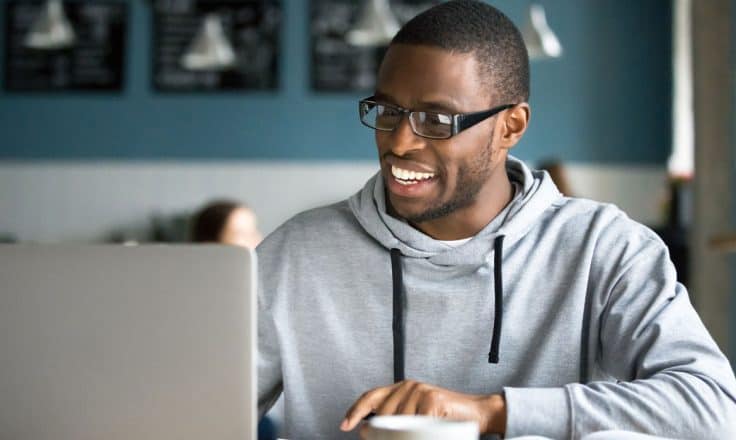 man in sweatshirt working on a laptop and drinking tea at a coffee shop