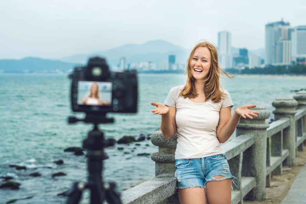 female travel blogger filming a travel video on a bridge with skyline behind her