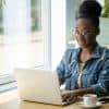 woman in denim jacket writing a blog post on her laptop at a coworking space