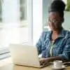 woman in denim jacket writing a blog post on her laptop at a coworking space