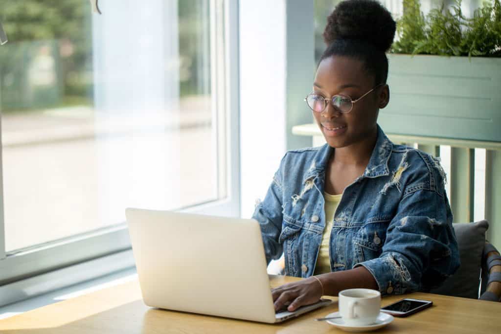 woman in denim jacket writing a blog post on her laptop at a coworking space