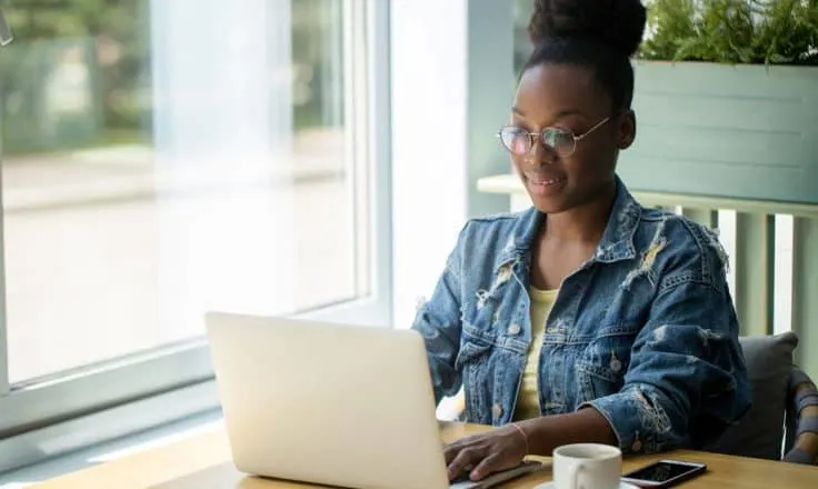 woman in denim jacket writing a blog post on her laptop at a coworking space