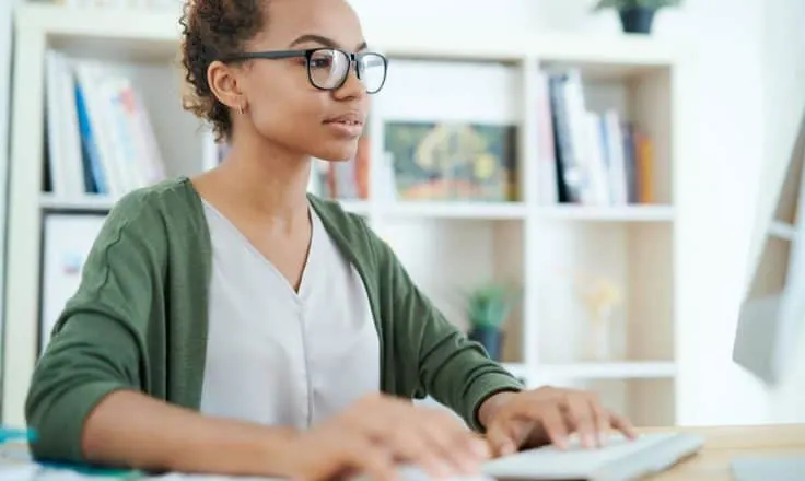 young woman wearing a green cardigan working on a desktop computer in a home office