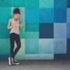 woman wearing headphones leaning against a colorful mural while looking at her phone