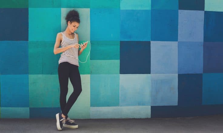 woman wearing headphones leaning against a colorful mural while looking at her phone