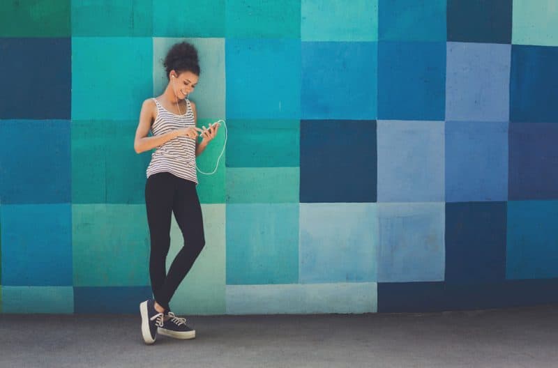 woman wearing headphones leaning against a colorful mural while looking at her phone