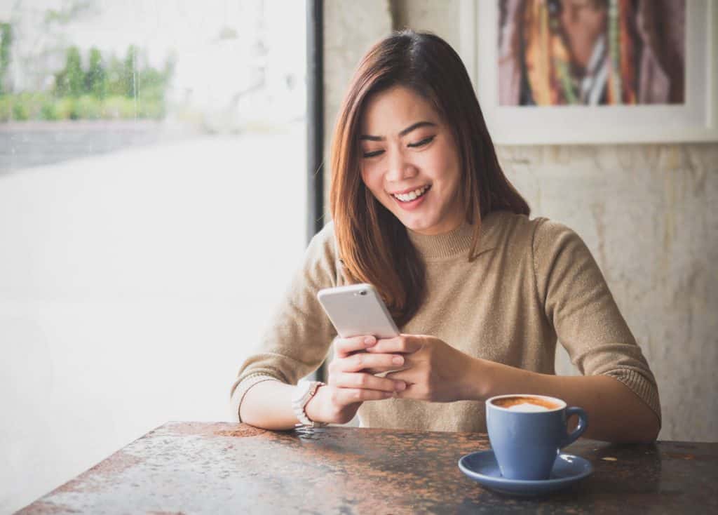 woman drinking coffee and looking at social media on her smartphone in a cafe