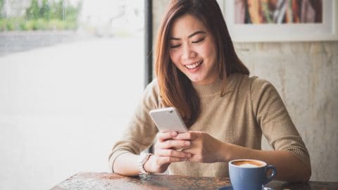 woman drinking coffee and looking at social media on her smartphone in a cafe