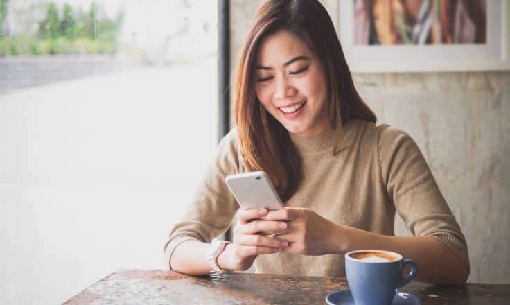 woman drinking coffee and looking at social media on her smartphone in a cafe