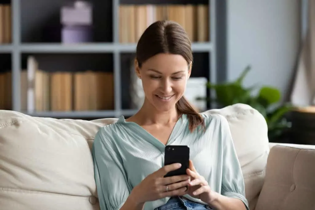 woman in light blue shirt looking at a smartphone on a couch in her home