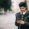 male blogger in leather jacket typing on his cell phone while walking on an empty street