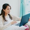 young woman working on her website from a laptop on her couch in her home