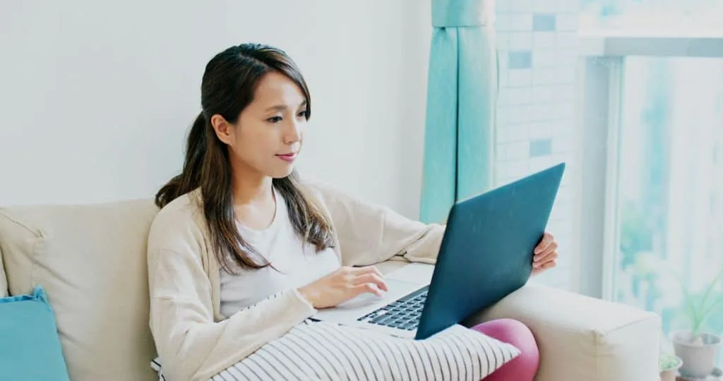 young woman working on her website from a laptop on her couch in her home