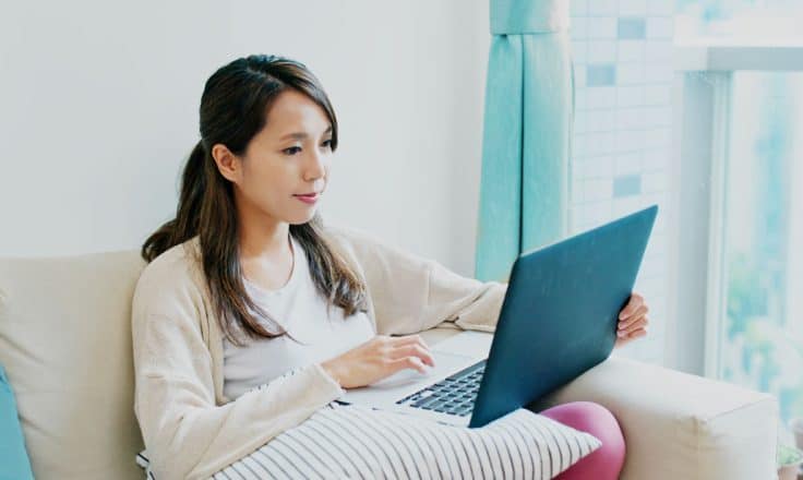young woman working on her website from a laptop on her couch in her home