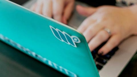 woman's hands typing on a teal computer covered in Mediavine stickers