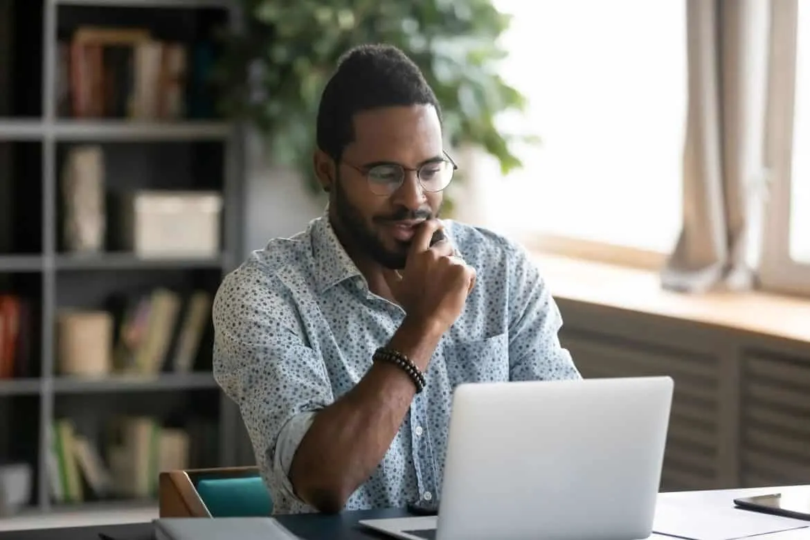 man in blue collared shirt working on a laptop in home office