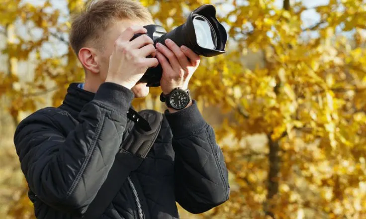 man looking through camera wearing a light jacket