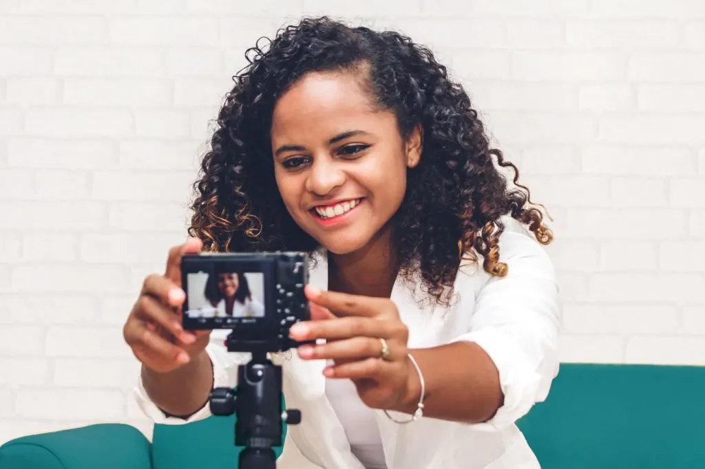 woman sitting on couch reaching to push a button on a camera facing her.