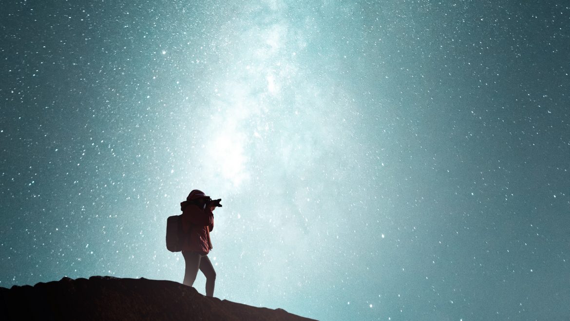 man taking photos of the night sky from the top of a hill