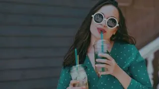female influencer in teal polka dot shirt drinking tea from a plastic cup