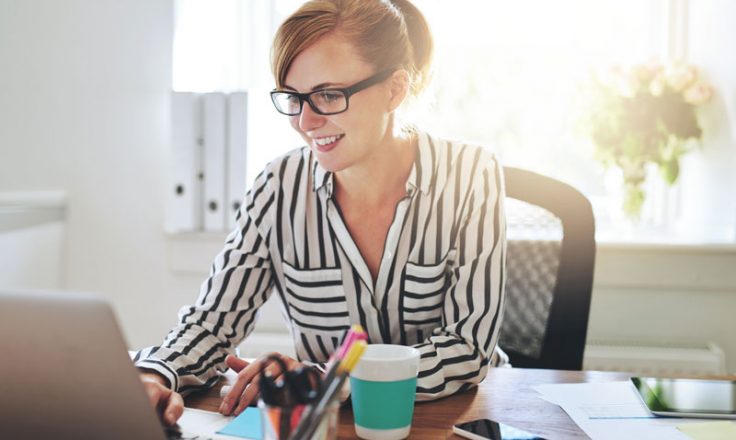 woman sitting at desk smiling at laptop