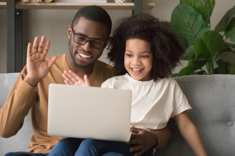 Dad and daughter waving to a computer on a video call