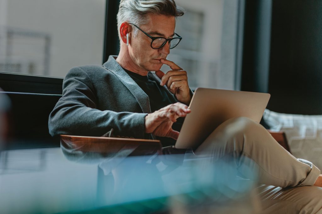 man in suit jacket working on a laptop in his lap in an office setting