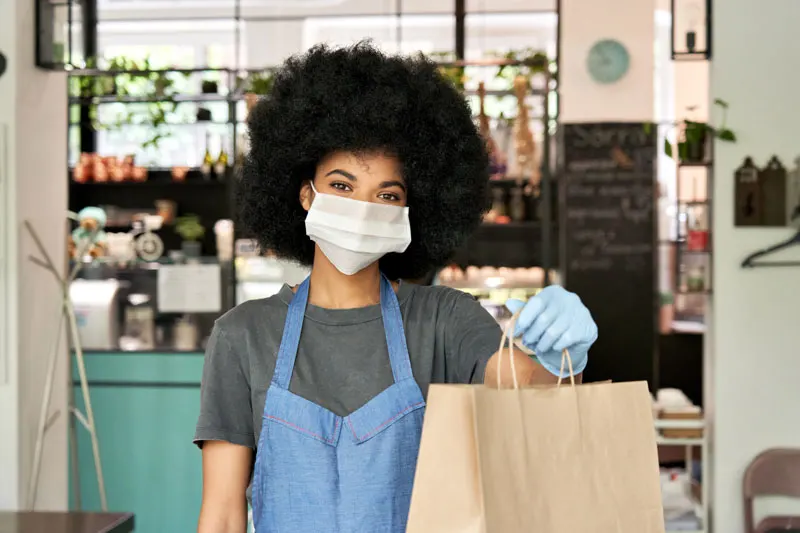 woman wearing mask holding up paper bag takeout pickup order