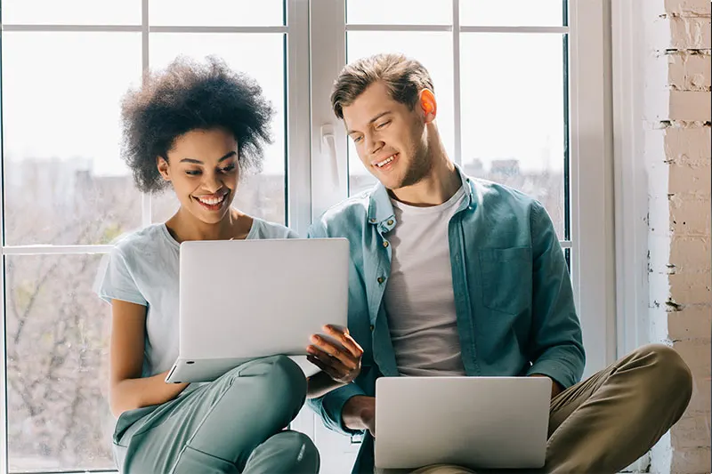 two people with laptops sitting on windowsill